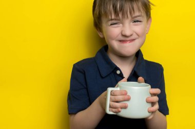 Avrupalı görünümlü bir çocuk elinde bir bardak içki tutuyor. Sarı arkaplan