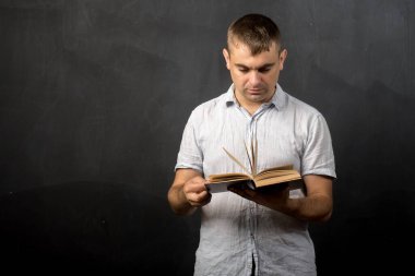 Genç bir erkek öğretmen karatahta duvarın önünde açık bir kitap tutuyor, metin ya da tasarım için yer sağlıyor. Öğrenme ve öğretme odaklı eğitim, okul veya sınıf kavramları için idealdir