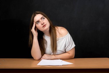 Masasında oturan genç bir kadın, önünde kağıtlarla derin düşüncelere dalmış. Yukarıya bakıyor, düşünüyor ya da hayal kuruyor. Yaratıcılık, problem çözme ya da eğitim gibi kavramlar için mükemmel bir sahne.