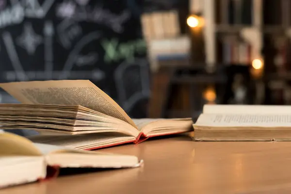 Tahta bir masada açık kitaplar ve havada sayfalar uçuşuyor. Bilgi, eğitim, edebiyat ve öğrenme kavramı. Dim arka plan entelektüel ve odaklanmış bir atmosfer yaratır