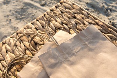 Kraft paper bags neatly stacked on a straw tray on a sandy beach. The warm tones of the beach setting emphasize eco-friendly products, highlighting sustainability and nature-friendly solutions clipart