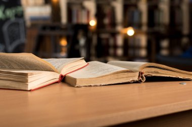 Open vintage books on a wooden table in a library, with softly blurred shelves in the background. A perfect image to evoke the warmth and charm of traditional reading spaces and literary exploration clipart