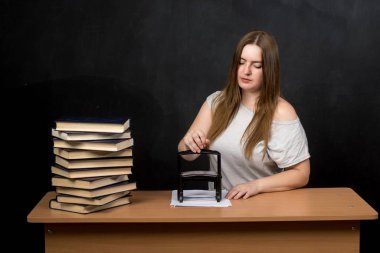 Yanında bir yığın kitapla masa başında evrakları damgalayan bir kadın. Bir ofiste ya da okul ortamında eğitim, yönetim ya da evrak işleri için mükemmel