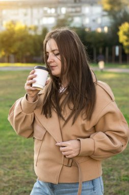 Elinde kahve fincanı tutan bej ceketli bir kadın, dikkatlice uzaktan bakıyor. Sonbahar temaları, rahatlama ve açık havada huzurlu anlar için mükemmel.