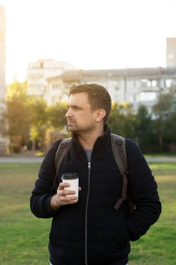 Bir adamın elinde kahve olan, akşamları stadyumda dikilen şehir manzarası. Arka plandaki yüksek binalar şehir yaşam tarzını geliştiriyor..