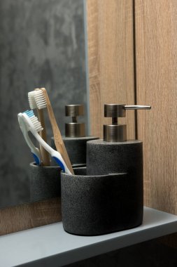 Siyah bir sabun makinesinin ve beyaz ve ahşap bir diş fırçasının olduğu bir diş fırçasının yakın çekimi. Arkaplanda tahta bir panel ve bir ayna var.. 