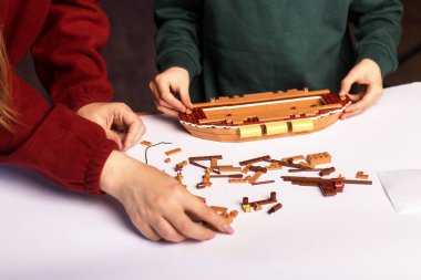 Two people assembling a model ship using building blocks on a white table. The partially assembled ship and various pieces are visible, showcasing the creative and engaging activity