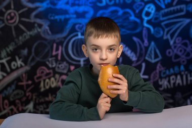 Elinde abur cuburla mutlu bir çocuk. Renkli bir karatahtanın yanında oturuyor. Okul resimleriyle birlikte. Okula dönüş, çocuk sağlığı ve eğitim kavramları için ideal.