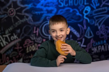 Topuzlu bir çocuk, renkli karalamalarla yazı tahtasının önünde oturuyor. Çocukluk teması, okul yemeği ve eğlenceli sınıf anları için harika..