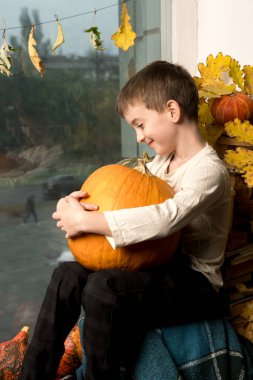 A young boy smiles while hugging a large pumpkin, with an autumn-themed background. Ideal for fall, seasonal celebrations, and harvest-themed concepts clipart