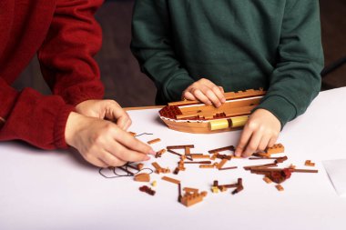 Çocuk duyarlı ve odaklı ahşap bir gemi modeli inşa ediyor, oyunculuk eğitimi, sabır ve çocukluk yaratıcılığını sembolize ediyor.