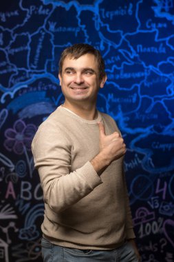 Gündelik bej kazaklı gülümseyen erkek öğretmen renkli bir yazı tahtasının önünde olumlu, destek ve eğitimi sembolize ediyor..