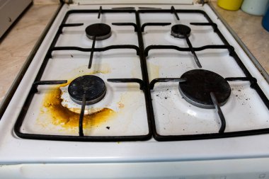 Kirli gaz sobası, yağ lekeleri ve yanmış gıda kalıntıları kullanılmış ve dağınık bir mutfak aletini gösteriyor. Temizlik, hijyen ve günlük ev işleriyle ilgili konular için mükemmel.