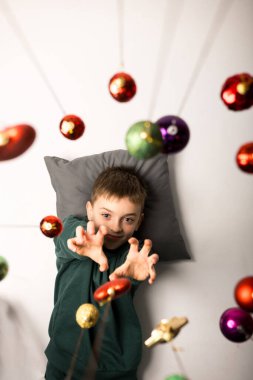 A person in a green outfit lying on a blue pillow with hanging Christmas ornaments, capturing a festive and tranquil moment. Perfect for holiday relaxation themes clipart