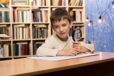 Kütüphanede elinde büyüteçle kitap ve bilgi dünyasını keşfeden küçük bir çocuk. Arkaplan kitaplıklarla dolu, eğitici bir atmosfer yaratıyor.