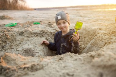 Kum oyununa dalmış, elinde oyuncak bir kürek tutan kaygısız çocukluk anlarını ve açık hava eğlencesini temsil eden genç bir çocuk. Eğitici, eğlenceli ve yaz temaları için harika.
