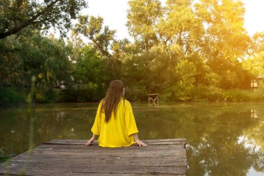 Back view of a woman on a pier enjoying the quiet and stillness of a forest lake. Warm sunlight filters through the trees, creating a sense of relaxation and mindfulness clipart