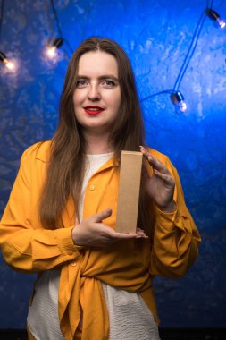 Person in a yellow shirt presenting a blank cardboard box in a professional studio setting. Perfect for product mockups, packaging design, and e-commerce visuals. clipart