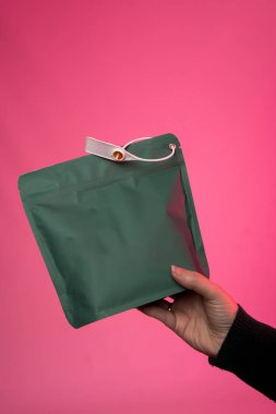 Canlı pembe arka planda beyaz plastik bir şarjörle yeşil, yeniden mühürlenebilir bir çanta tutuyor. Metin veya reklam için geniş bir alanı olan ambalaj, depolama ve markalaşma kavramları için ideal