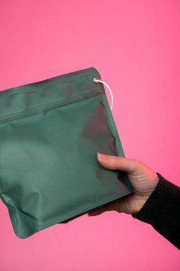 Canlı pembe arka planda beyaz plastik bir şarjörle yeşil, yeniden mühürlenebilir bir çanta tutuyor. Metin veya reklam için geniş bir alanı olan ambalaj, depolama ve markalaşma kavramları için ideal