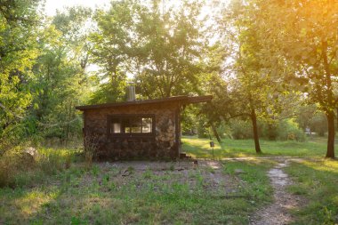 Bereketli yeşil ormandaki ahşap kulübe, sıcak güneş ışığıyla yıkanmış. Huzurlu bir dinlenme yeri arayan doğa aşıkları için mükemmel, kırsal cazibe ve doğal güzellik sergiliyor.
