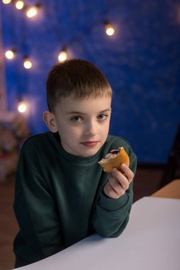 Ellerinde çörek olan, yemek yerken düşünceli görünen bir öğrenci. Çocuk yemekleri, beslenme ya da eğitim ortamları hakkında içerik için mükemmel.
