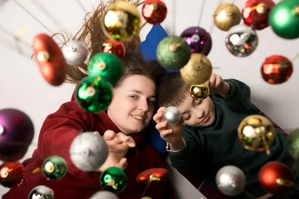 Gülümseyen anne ve çocuğu Noel 'in tadını çıkarıyorlar. Parlak Noel süsleriyle çerçevelenmiş. Aile, aşk ve kutlama temaları için mükemmel..