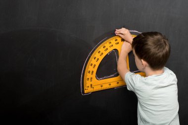 Tahtaya çizim yapmak için büyük sarı bir kare kullanan bir çocuk, hassasiyet ve geometri üzerine odaklanıyor. Eğitim ve okulla ilgili konular için mükemmel