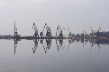 Vinçleri ve sudaki yansımaları olan sakin endüstriyel liman. Endüstriyel güzelliğin ve huzurun özünü yakalıyor.
