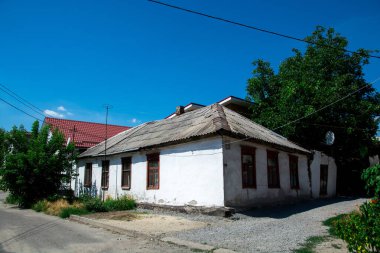 Yeşillik ve açık mavi gökyüzü ile çevrili, yıpranmış çatısı ve ahşap pencereleri olan eski bir kır evi. Kırsal cazibe ve kırsal yaşam için mükemmel bir tasvir.