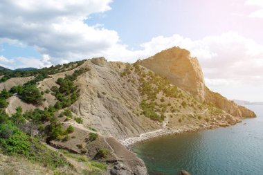 Kıyı manzarası kayalık tepeler, seyrek bitki örtüsü, berrak mavi-yeşil su ve kıyıya yakın teknelerle çevrili. Seyahat, doğa ve açık hava temaları için mükemmel.
