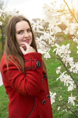 Portrait of a young lady in a stylish red coat surrounded by white magnolia flowers. Perfect for concepts of spring, beauty, and elegance clipart