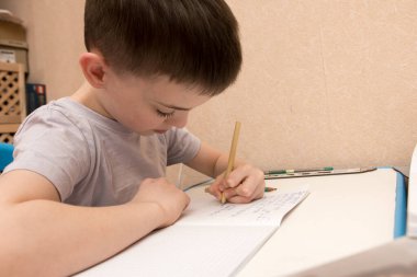 Masaya not defterine yazı yazan solak bir çocuk. Çocuk elinin kalem tutmasına ve kare kağıda yazmasına odaklanmış durumda. Eğitim veya öğrenmeyle ilgili konular için mükemmel