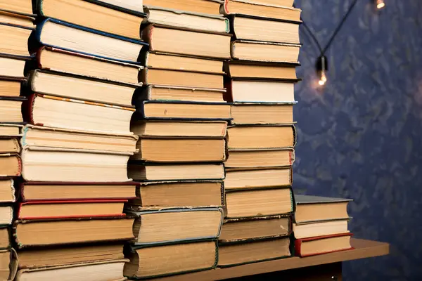 Masaya dizilmiş kitaplar ve dokulu mavi bir duvarda parlayan sicim lambaları. Eğitime, nostaljiye ya da iç tasarım görsellerine uygun rahat ve çalışkan bir atmosfer yakalar.