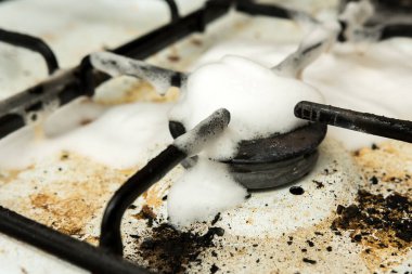 Yanmış besin kalıntısı ve temizlik köpüğüyle dolu pis bir gaz ocağı. Gerçek hayatta mutfak bakımı, hijyen mücadelesi ve derin temizlik görevlerinin bir temsili.