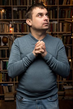 Kitap dolu bir odada elleri dua ederken sımsıkı bağlanmış, yukarıyı seyreden rahat bir kazak giyen bir adam. Ruhaniliğin sembolü, bilgelik, cevaplar aramak, ya da derin tefekkür..