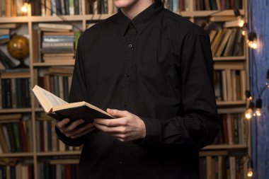 Siyah gömlekli bir adam kütüphanede kitap okuyor, kitaplıklarla çevrili, eğitim, edebiyat veya akademik ilham için ideal..