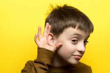 Dikkatle dinleyen çocuk, eli kulağına kenetlenmiş, sarı arka plan. Dinleme, öğrenme, merak ve çocukluk iletişimi konuları için harika.