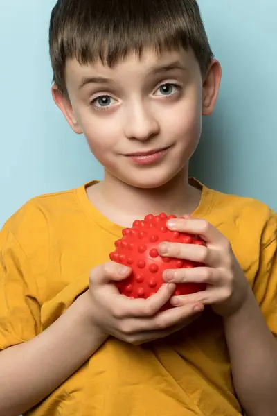 Kırmızı dikenli top tutan sarı tişörtlü çocuk. Oyun, çocukluk, duyusal aktiviteler ve eğlence için idealdir..