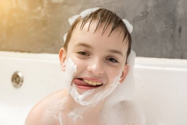 Köpükle kaplı gülümseyen çocuk küvette oynar, tıraş olmuş numarası yapar. Samimi bir banyoda eğlenceli, kaygısız bir çocukluk anı. Günlük hayatta mutluluk ve neşe.