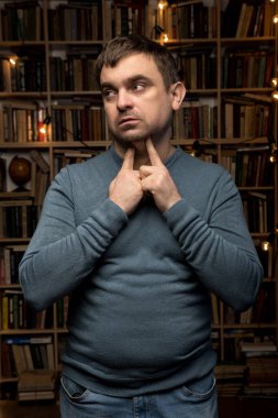 Meraklı bir adam, kitaplarla çevrili, boğazına jest yapıyor, yumuşak bir arka plan, deniz mavisi ve kot