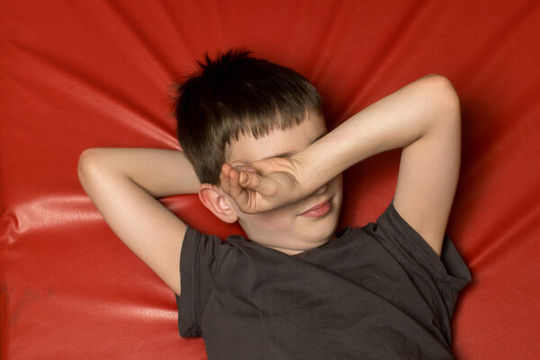 Милый ребенок отдыхает на красном коврике, игриво закрывая глаза ухмылкой. Идеально подходит для радости, молодости и игровых моментов на складе.