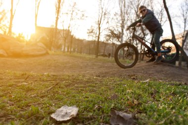 Bisikletçi gün batımında bir parkta çamurlu bir yolda gidiyor. Önünde çimenler ve ağaçlar var. Açık hava sporları, doğa ve eğlence fotoğrafçılığı için mükemmel..