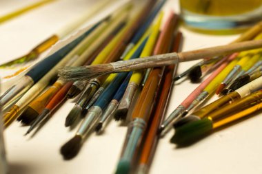 Renkli tutacakları olan boya fırçaları koleksiyonu ve beyaz arka planda sarı boya kavanozu, tatil sanatı ve bahar esinlenilmiş DIY el işi seansları için ideal..