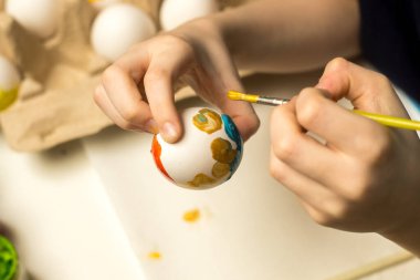 Eller, boyalı yumurta ve fırçalarla çevrili parlak tonlu bir Paskalya yumurtasını dikkatlice boyar. Paskalya gelenekleri, yaratıcı aktiviteler ya da tatil eğlenceleri için harika..