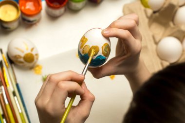 Eller, yumurta ve sanat malzemeleriyle çevrili bir fırça kullanarak canlı renklerle bir Paskalya yumurtası boyarlar. Tatil sanatları, yaratıcılık ve festival teması için mükemmel..