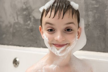 Kafasında köpük, vücudunda küvette gülümseyen mutlu bir çocuk. Eğlenceli banyo zamanı, hijyen ve çocukluk anları kavramı.