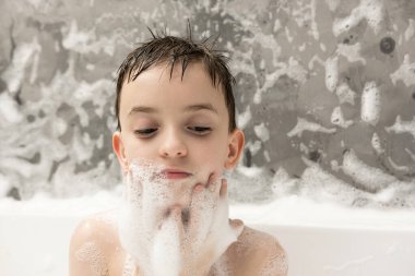 Kafasında şampuan köpüğü ve küvette vücudunda hafifçe gülümseyen sevimli bir çocuk. Banyo zamanı eğlence, temizlik ve günlük bakım..