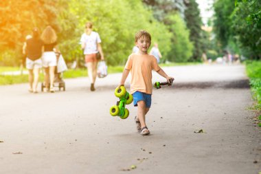 Neşeli bir çocuk güneşli bir parkta uzaktan kumandalı bir arabayla oynar. Neşeli ifadesi ve yaz kıyafetleri bu eğlenceli anı vurguluyor..
