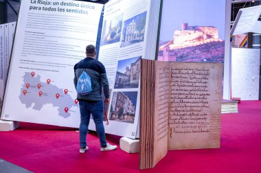 25 Ocak 2025; Madrid; İspanya: Bir turizm fuarında La Rioja hakkında geniş bilgi panelleri okuyan mavi sırt çantalı bir adam.